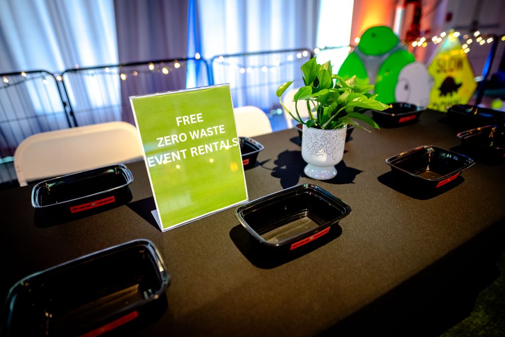 Reusable food service supplies sit on a table with a sign.