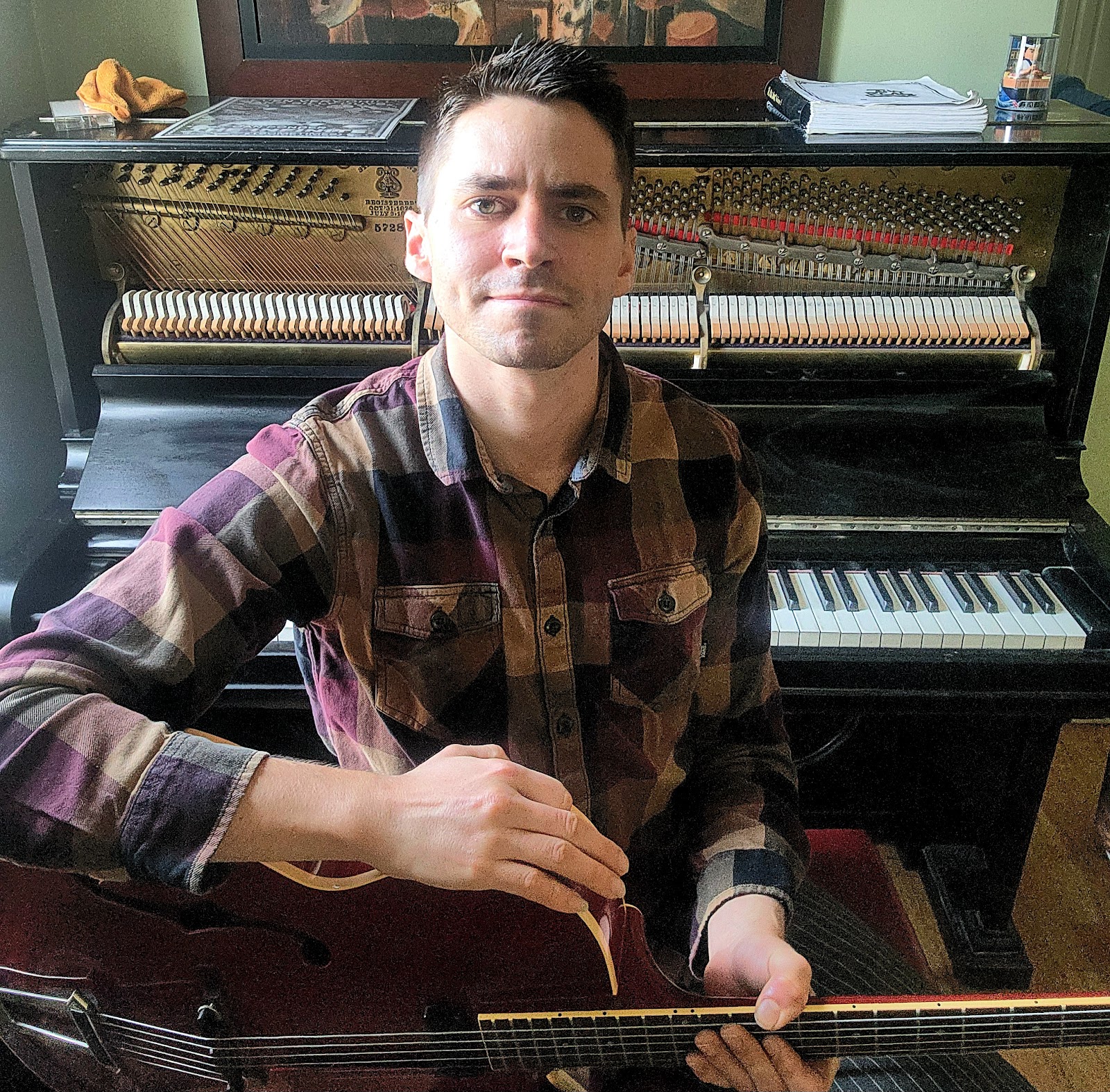 Ben Woodman with a guitar, piano in the background