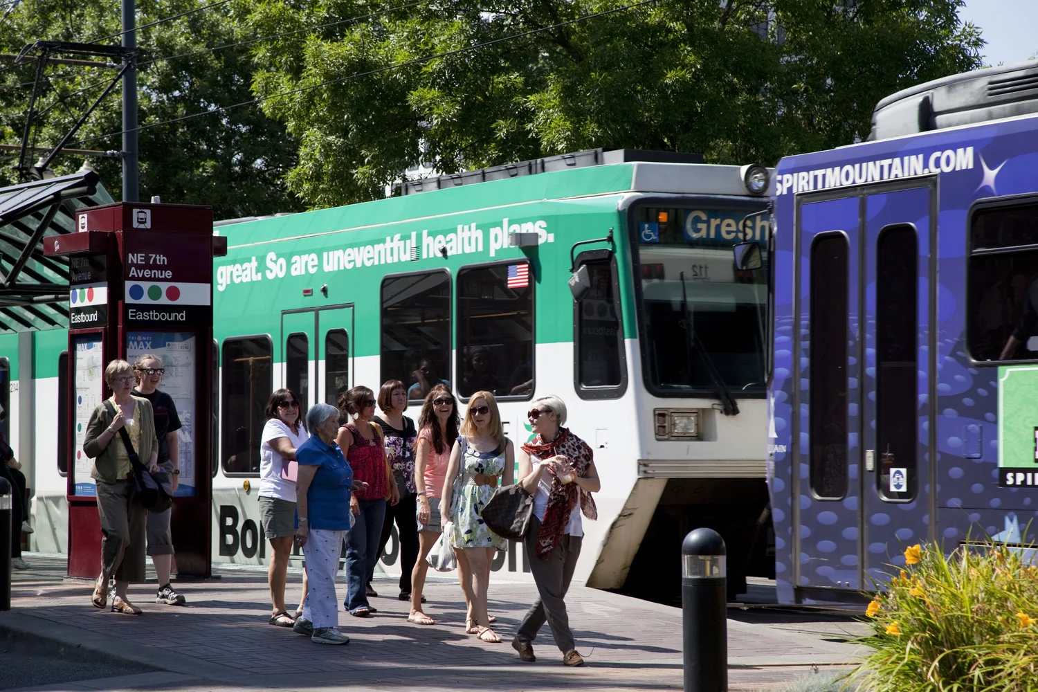 A group of people at a MAX stop with a passing MAX train car in the background