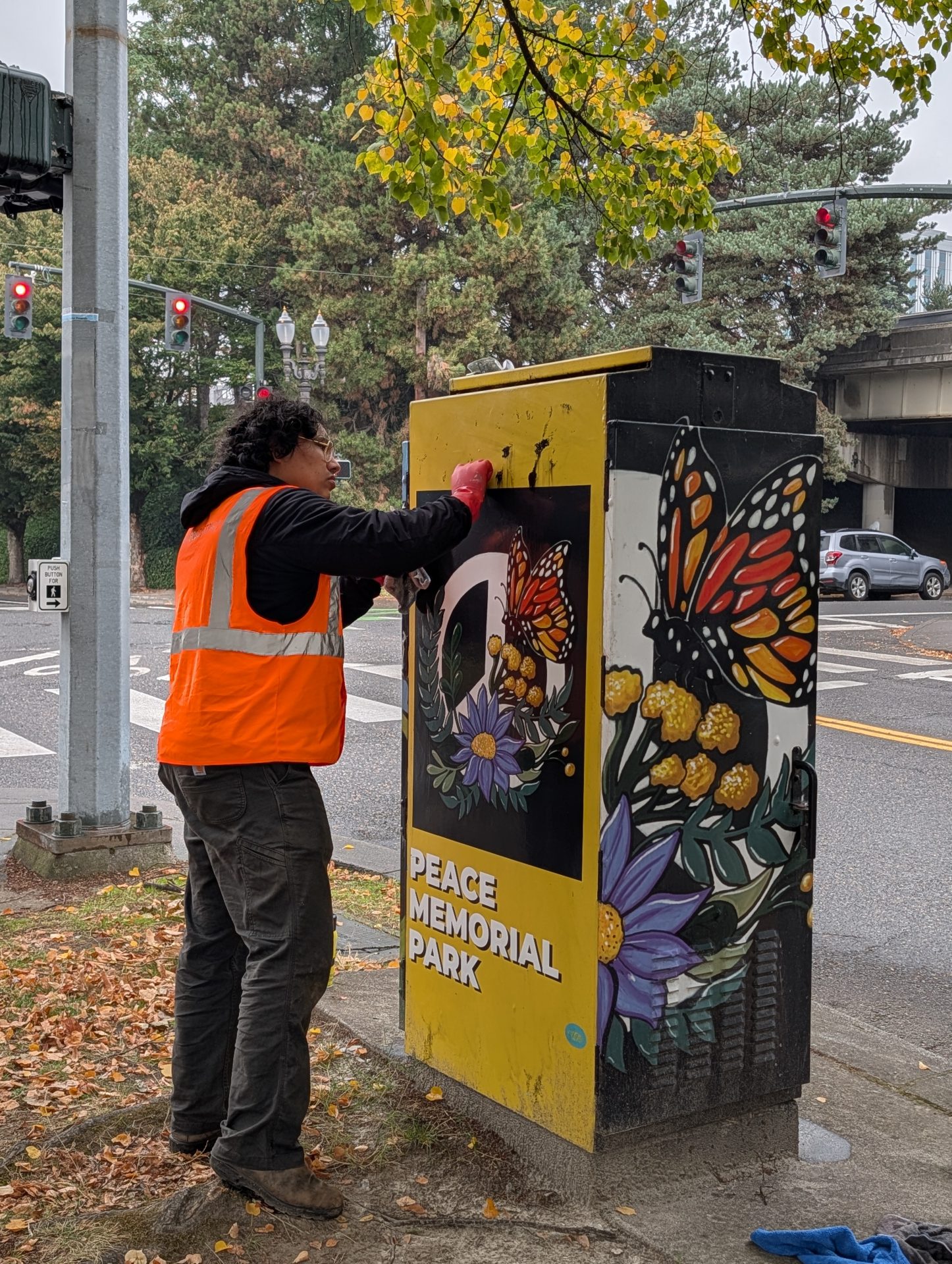A photo of a volunteer in a safety vest scrubbing graffiti of artwork in Peace memorial park.