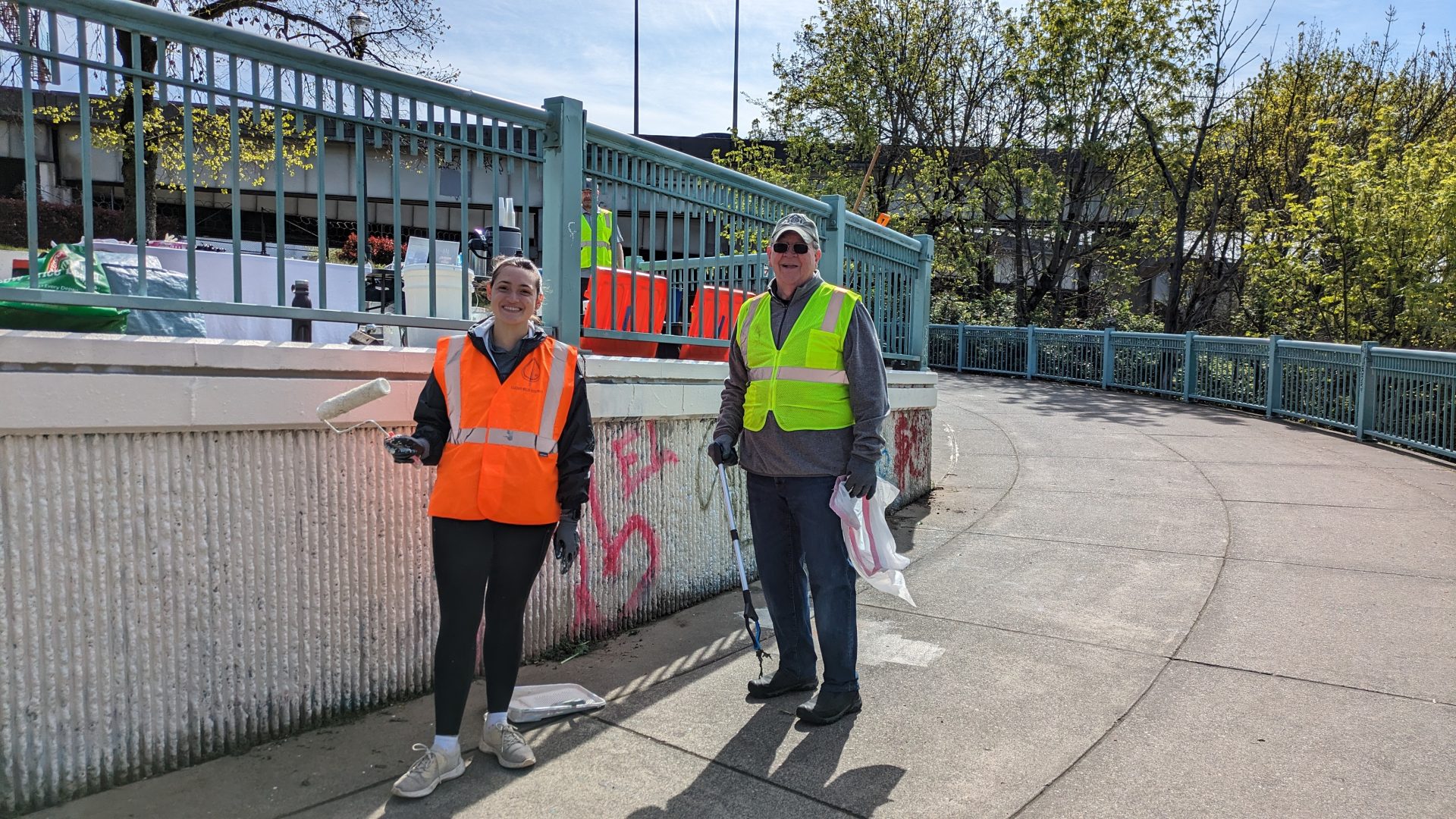 Two people posing in front of a fence at Peace Memorial Park, showing their cleanup progress.