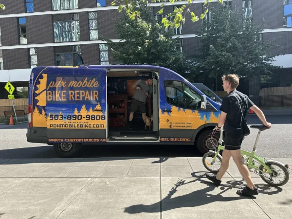 A PDX Mobile Bike Repair van with a biker walking up to it from the right