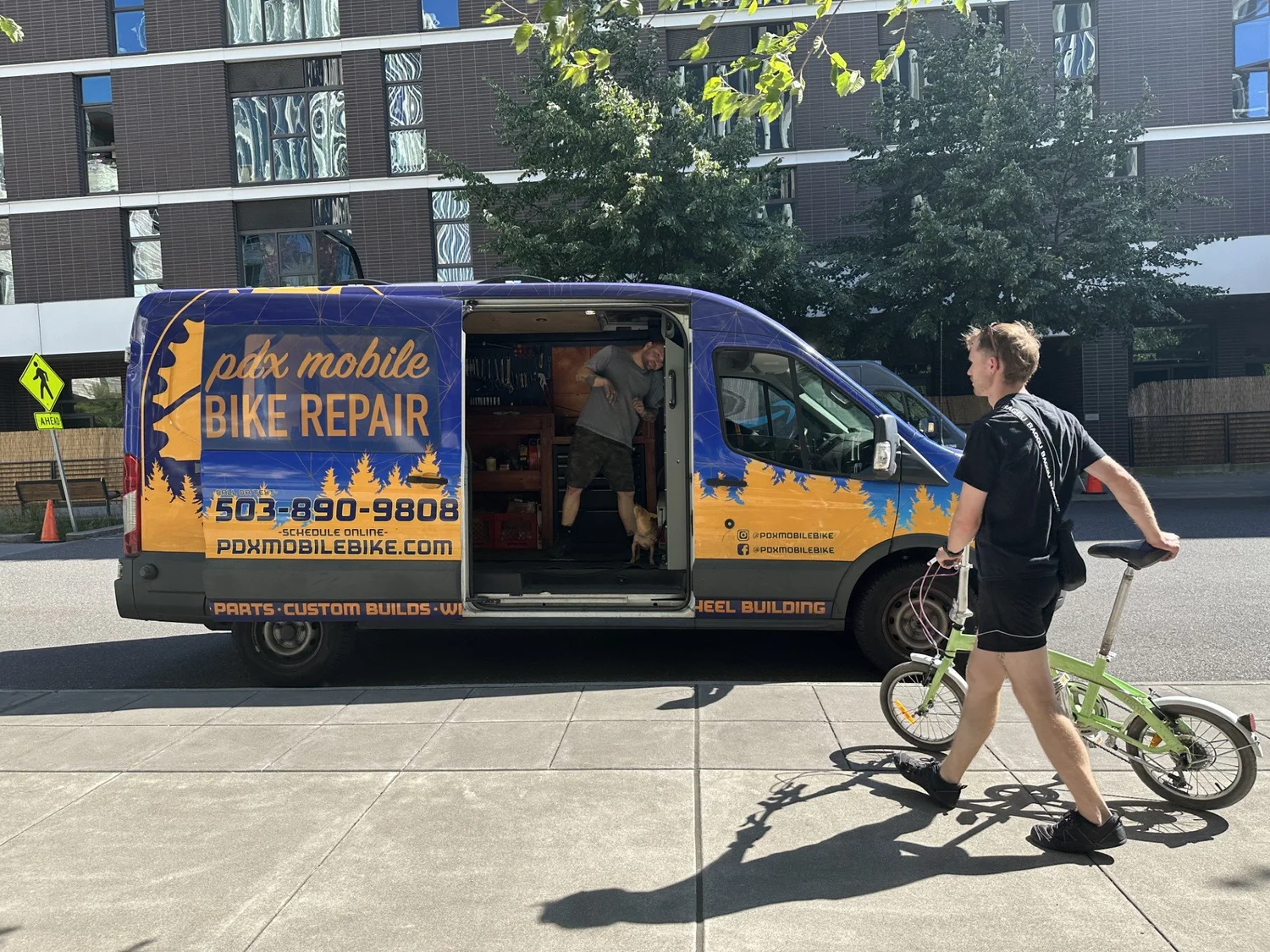 A PDX Mobile Bike Repair van with a biker walking up to it from the right