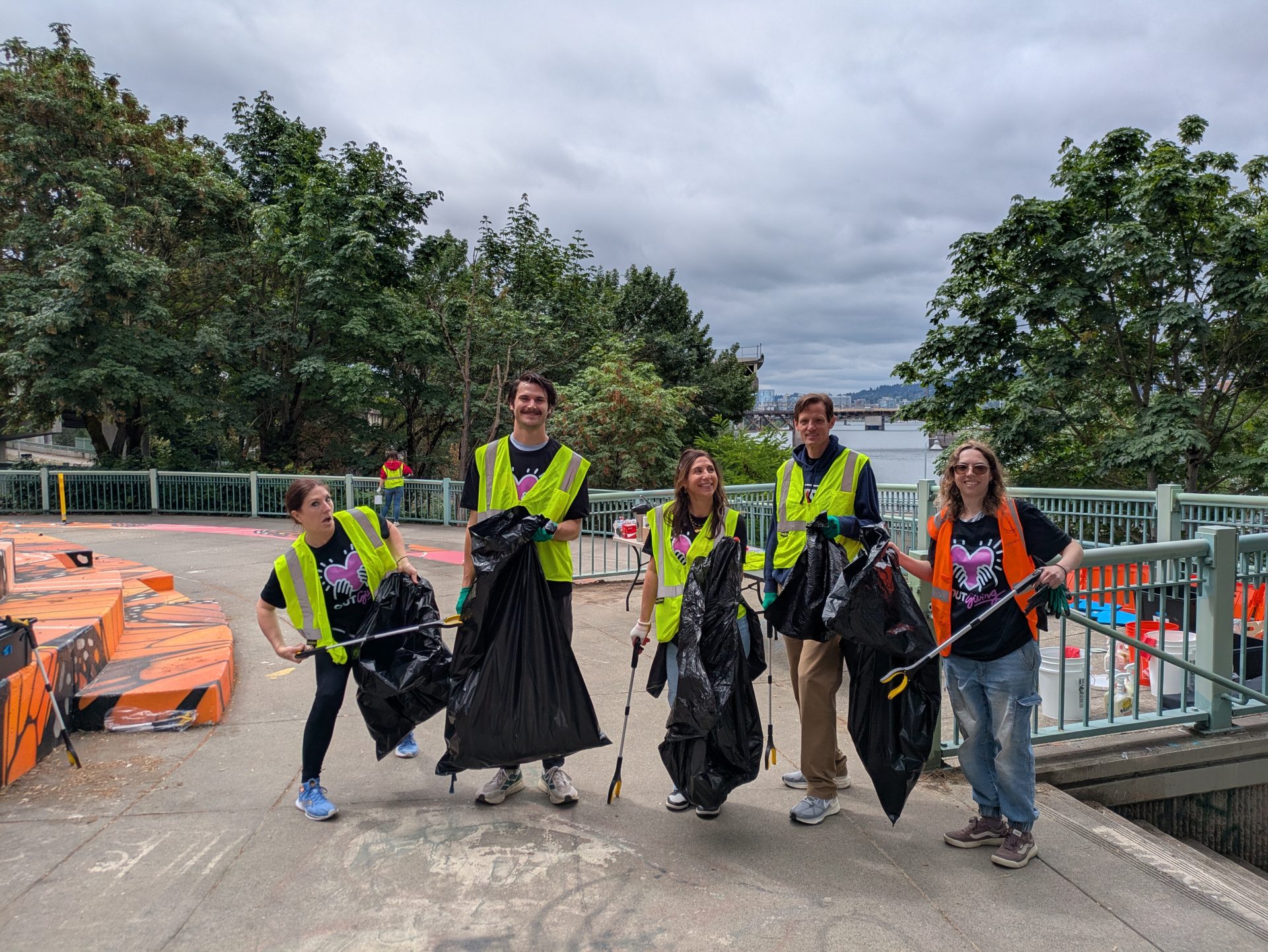 Five volunteers in vest and holding garbage bags pose for a photo at Peace Memorial Park