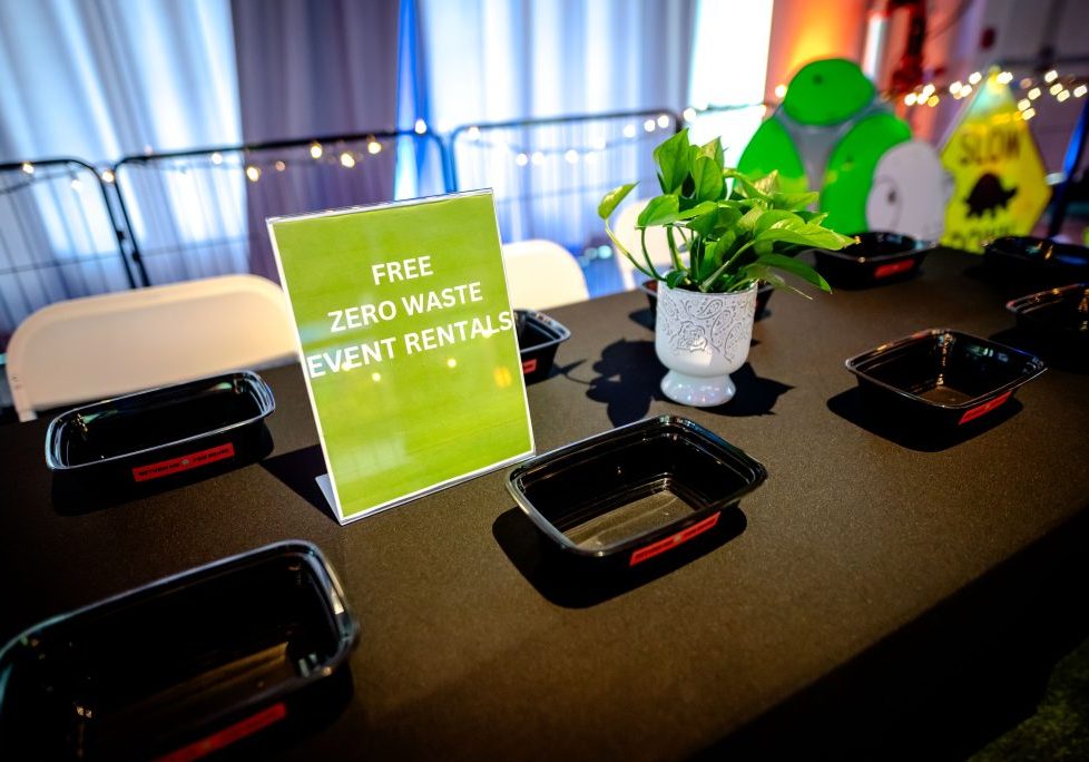 Reusable food service supplies sit on a table with a sign.