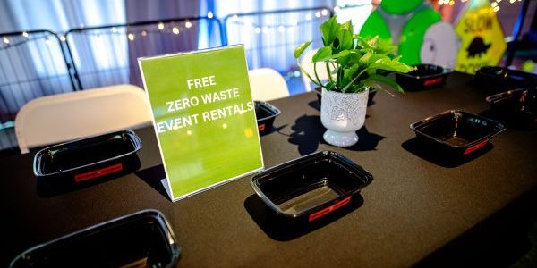 Reusable food service supplies sit on a table with a sign.