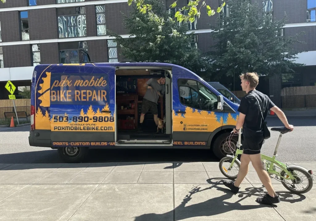A PDX Mobile Bike Repair van with a biker walking up to it from the right
