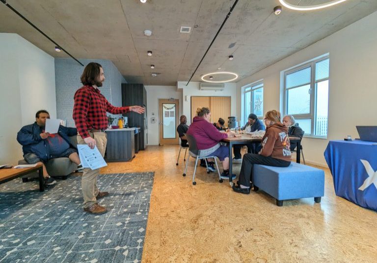 a photo taken during a financial wellness workshop that how a man standing in front of group of individuals sitting down looking over materials.