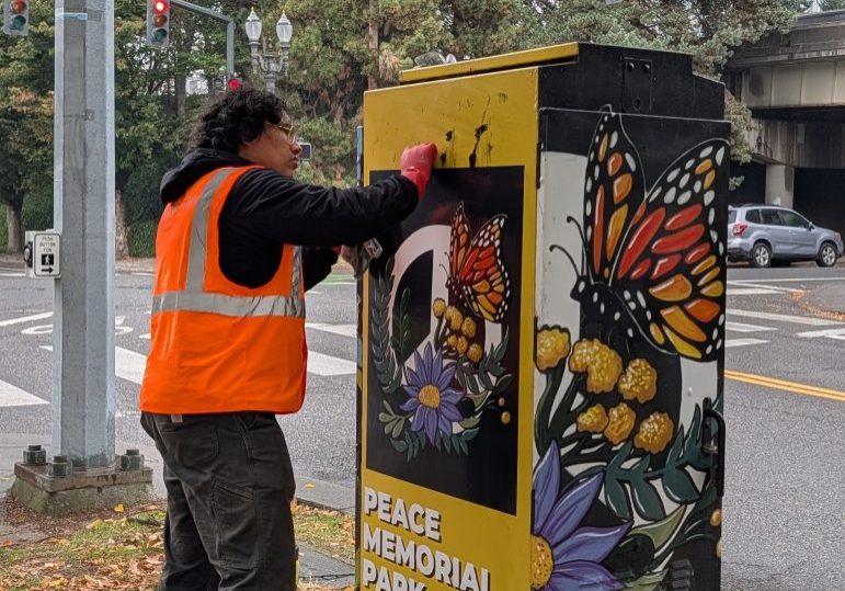 A photo of a volunteer in a safety vest scrubbing graffiti of artwork in Peace memorial park.