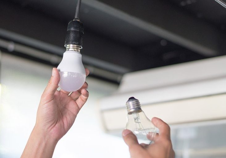 Power saving concept. Asia man changing compact-fluorescent (CFL) bulbs with new LED light bulb.