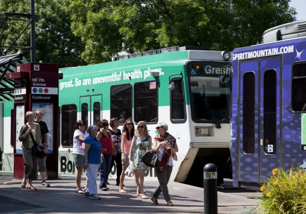 A group of people at a MAX stop with a passing MAX train car in the background
